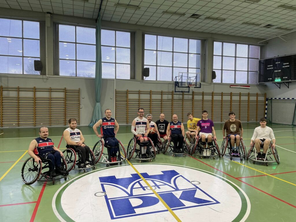 Studenci oraz koszykarze na wózkach pozują do zdjęcia na hali sportowej