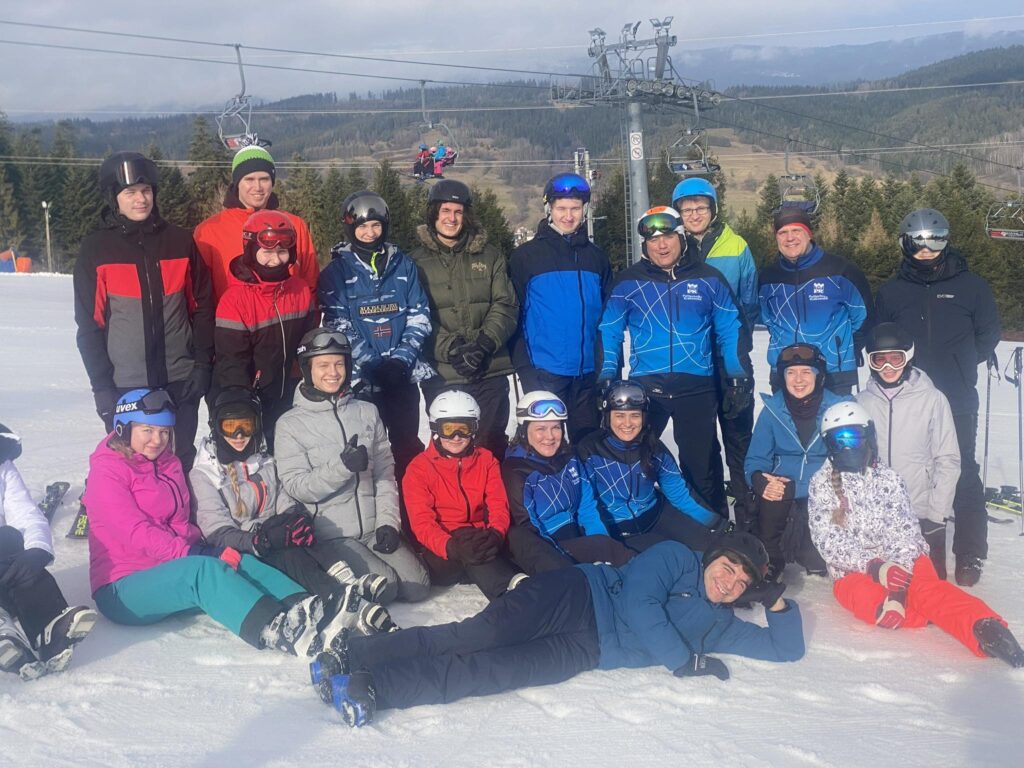 Studenci i instruktorzy pozują do zdjęcia na tle stoku narciarskiego