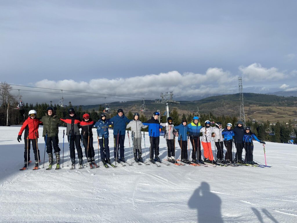 Grupa narciarzy stoi w rzędzie na stoku narciarskim i trzyma się za ramiona