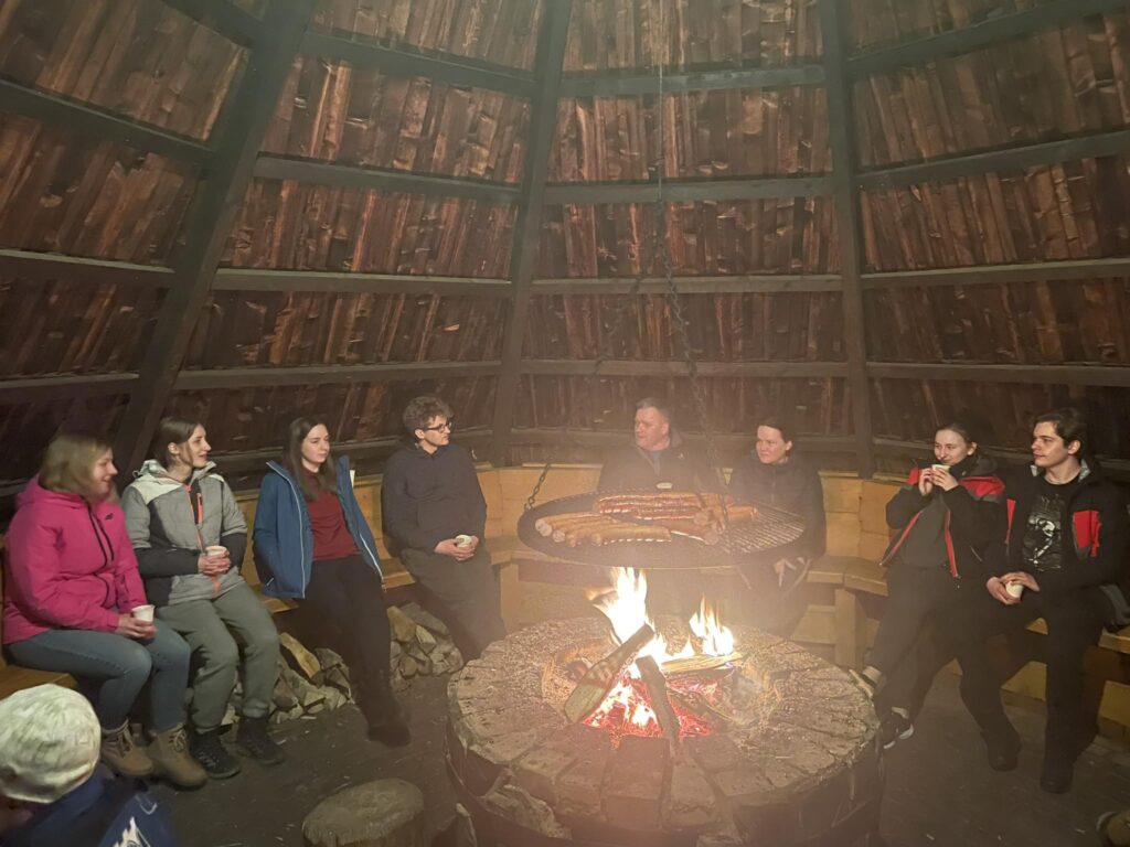 Uczestnicy obozu siedzą przy ognisku w wiacie